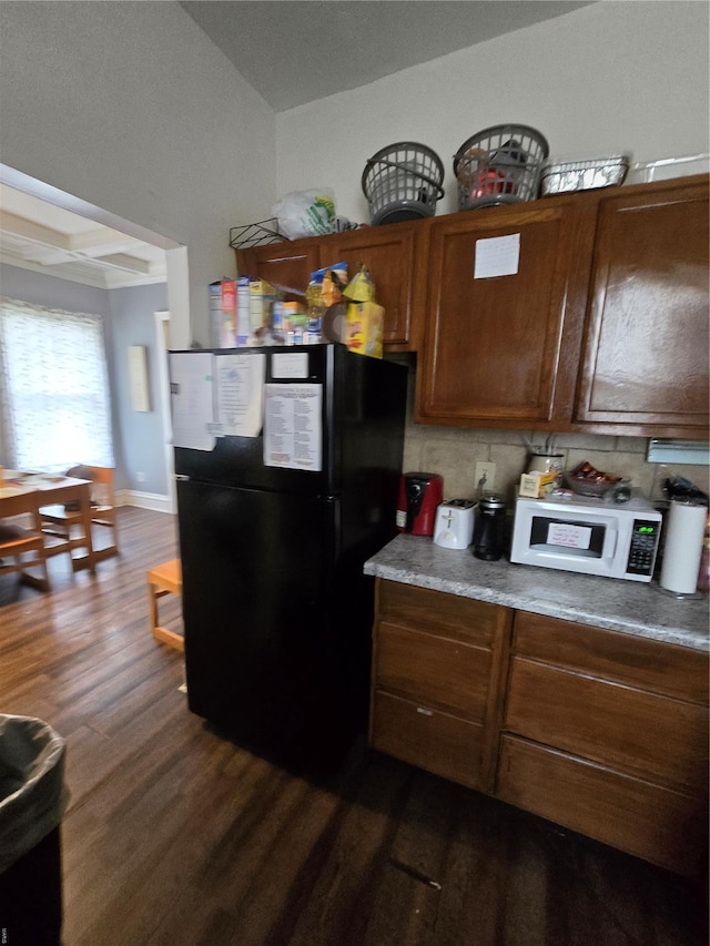 kitchen featuring white microwave, freestanding refrigerator, brown cabinetry, light countertops, and dark wood-type flooring