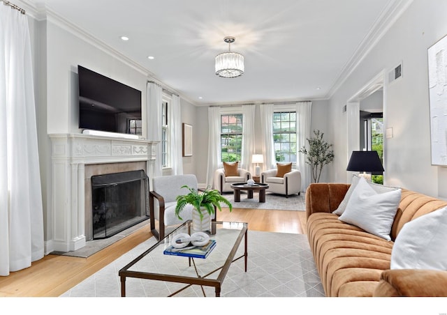 living room featuring visible vents, ornamental molding, a fireplace, and light wood finished floors