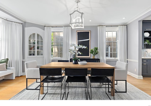 dining area with light wood-style floors, crown molding, and plenty of natural light