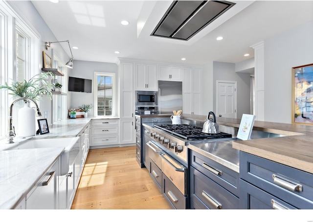 kitchen with built in appliances, white cabinetry, light wood-style floors, and a sink