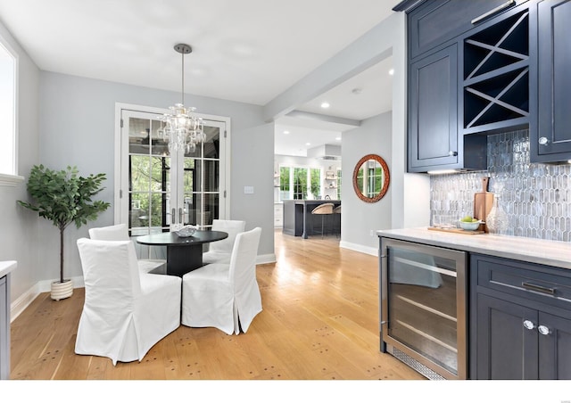 dining space featuring bar area, beverage cooler, light wood-style floors, and baseboards