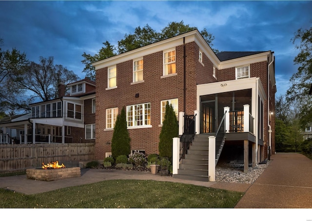 view of front of property featuring a sunroom, stairs, brick siding, a fire pit, and fence