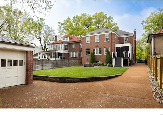 rear view of house featuring brick siding, fence, and a lawn