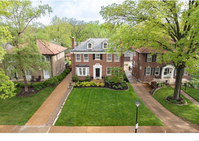 georgian-style home with a chimney, a front yard, and brick siding
