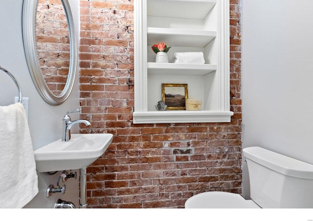 half bathroom featuring brick wall, toilet, and built in shelves