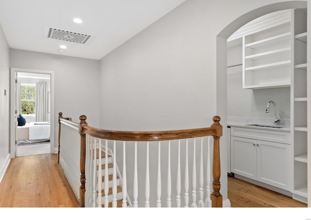 hallway featuring arched walkways, an upstairs landing, light wood finished floors, a sink, and visible vents