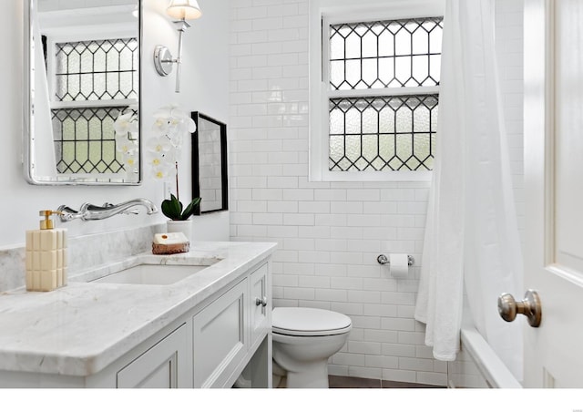 full bath with toilet, tile walls, shower / bath combo with shower curtain, and vanity
