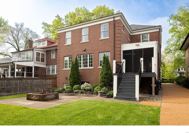 back of property featuring a sunroom, an outdoor fire pit, a yard, brick siding, and fence
