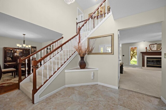 stairway featuring a high ceiling, a notable chandelier, a glass covered fireplace, and baseboards