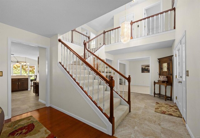 stairs with an inviting chandelier, wood finished floors, a towering ceiling, and baseboards