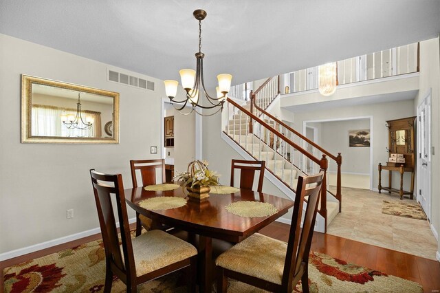 dining room featuring wood finished floors, visible vents, baseboards, a chandelier, and stairs