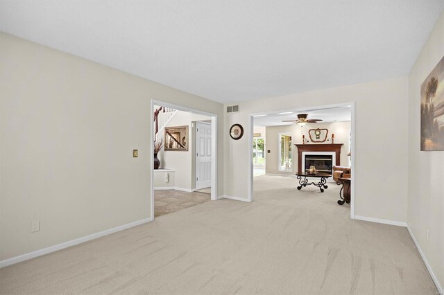 interior space with visible vents, baseboards, a glass covered fireplace, light colored carpet, and a ceiling fan