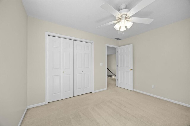 unfurnished bedroom featuring baseboards, visible vents, light colored carpet, a ceiling fan, and a closet