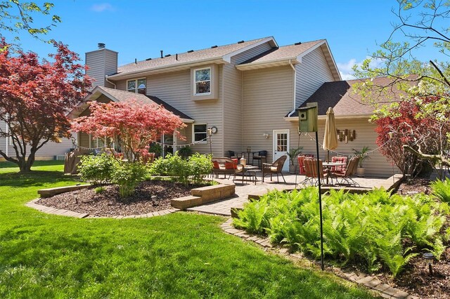 back of house featuring roof with shingles, a chimney, an outdoor hangout area, a yard, and a patio