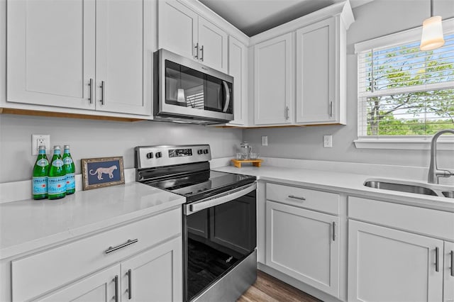 kitchen featuring hanging light fixtures, a sink, stainless steel appliances, white cabinets, and light countertops