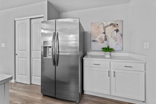 kitchen featuring light wood-style floors, light countertops, stainless steel fridge, and white cabinets
