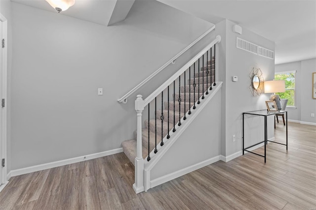 staircase with baseboards, visible vents, and wood finished floors