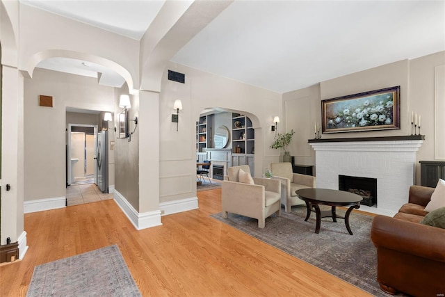 living area with visible vents, a fireplace, baseboards, built in shelves, and light wood finished floors
