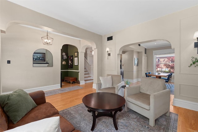 living room with stairway, arched walkways, baseboards, and light wood finished floors