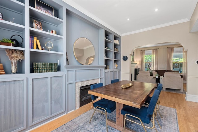 dining area with crown molding, light wood finished floors, a fireplace, arched walkways, and built in shelves