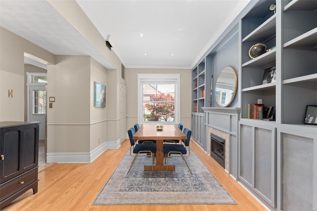 dining area featuring crown molding, a fireplace, built in shelves, baseboards, and light wood-style floors