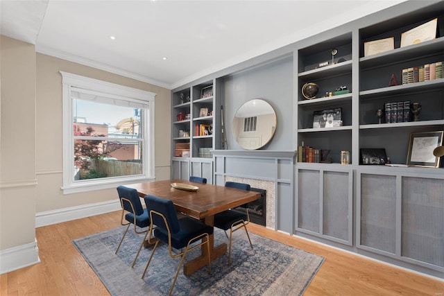 dining room featuring crown molding, a fireplace, built in shelves, wood finished floors, and baseboards