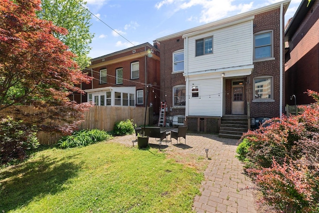 rear view of house featuring brick siding, fence, a yard, and entry steps