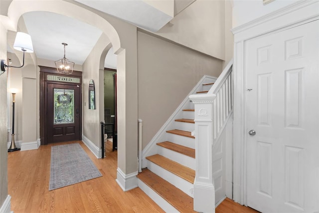 foyer featuring stairs, baseboards, arched walkways, light wood-style flooring, and a notable chandelier