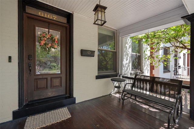 doorway to property featuring a porch and brick siding