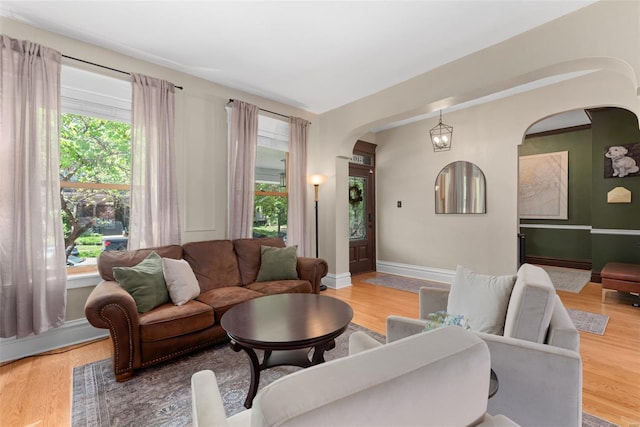 living area featuring a healthy amount of sunlight, arched walkways, baseboards, and light wood finished floors