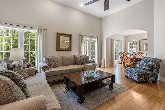 living area featuring a towering ceiling, arched walkways, hardwood / wood-style flooring, baseboards, and ceiling fan with notable chandelier