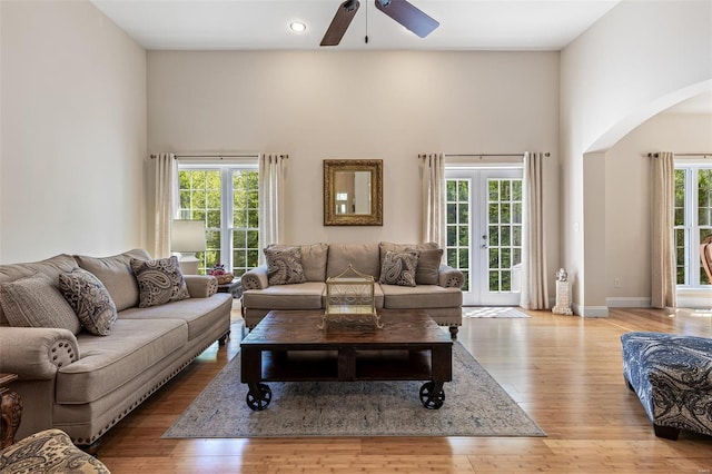 living area featuring arched walkways, a ceiling fan, wood finished floors, and a towering ceiling