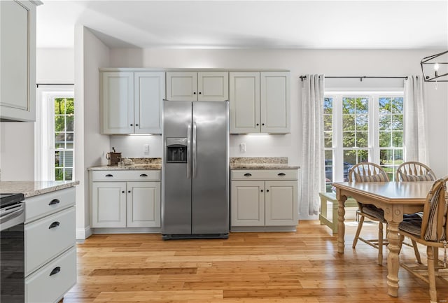 kitchen with stainless steel refrigerator with ice dispenser, electric range, a healthy amount of sunlight, and light wood-style floors