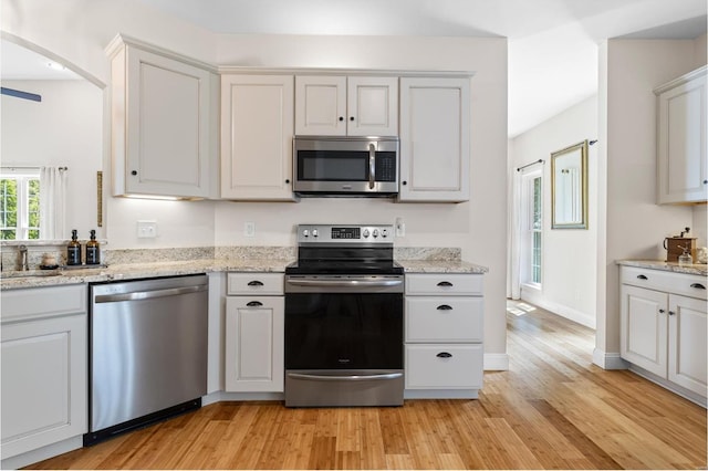 kitchen with light stone countertops, appliances with stainless steel finishes, light wood finished floors, arched walkways, and baseboards