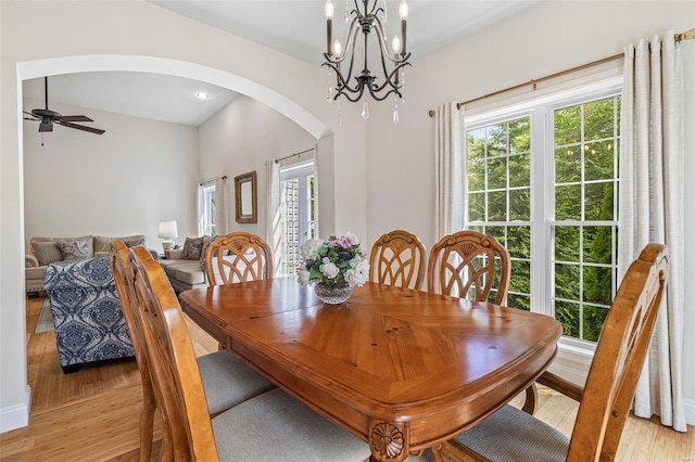 dining area with arched walkways, light wood-style flooring, and ceiling fan with notable chandelier