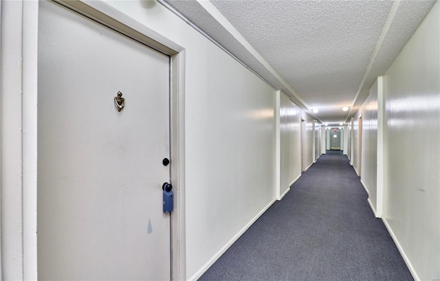 corridor with dark colored carpet, a textured ceiling, and baseboards