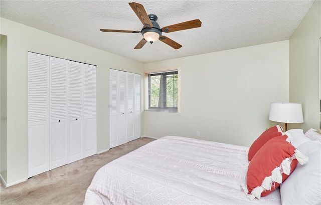 bedroom with multiple closets, ceiling fan, carpet flooring, baseboards, and a textured ceiling