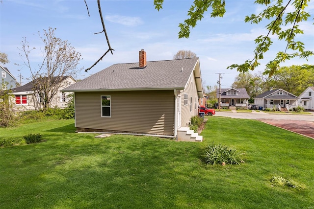 back of house with a lawn, roof with shingles, and a chimney