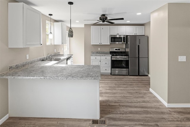kitchen featuring white cabinets, a sink, stainless steel appliances, wood finished floors, and a peninsula