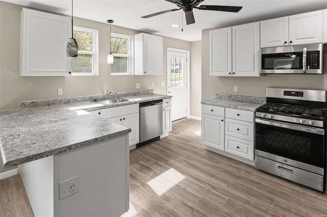 kitchen featuring stainless steel appliances, a sink, white cabinetry, a ceiling fan, and a peninsula