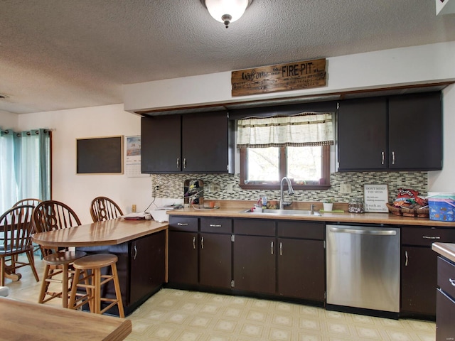kitchen featuring a sink, a textured ceiling, backsplash, light floors, and dishwasher