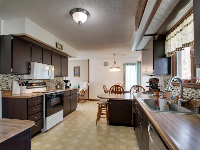 kitchen featuring a sink, white microwave, backsplash, electric range oven, and light floors