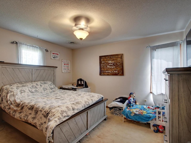 bedroom with a textured ceiling, ceiling fan, visible vents, and light carpet