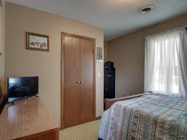 carpeted bedroom with visible vents, a textured ceiling, and a closet