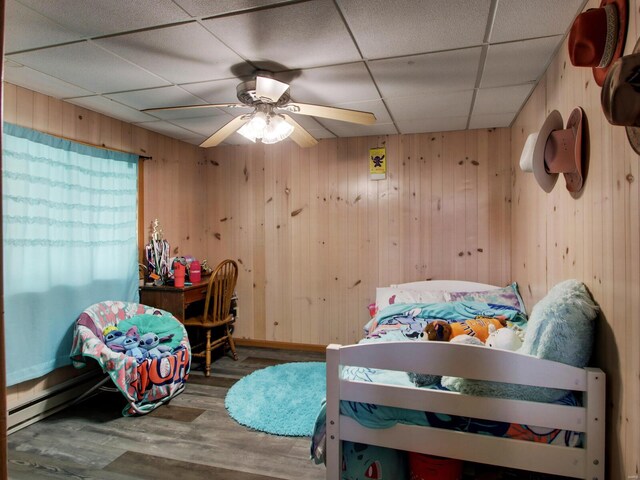 bedroom with wood walls, a ceiling fan, wood finished floors, and a paneled ceiling