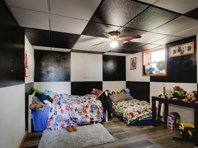 bedroom with ceiling fan, wood finished floors, and a paneled ceiling