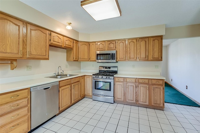 kitchen with a sink, appliances with stainless steel finishes, light tile patterned flooring, and light countertops