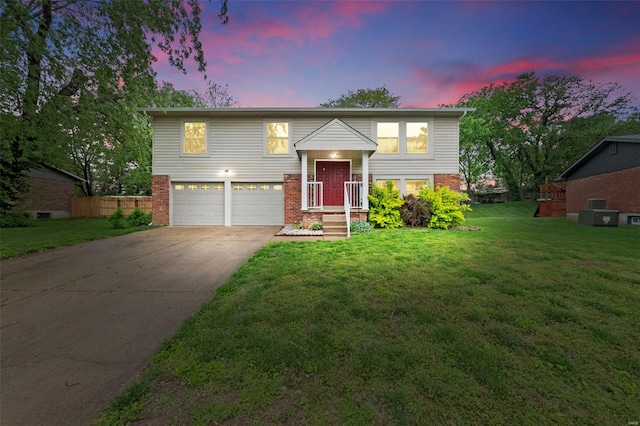raised ranch featuring concrete driveway, brick siding, a front yard, and a garage