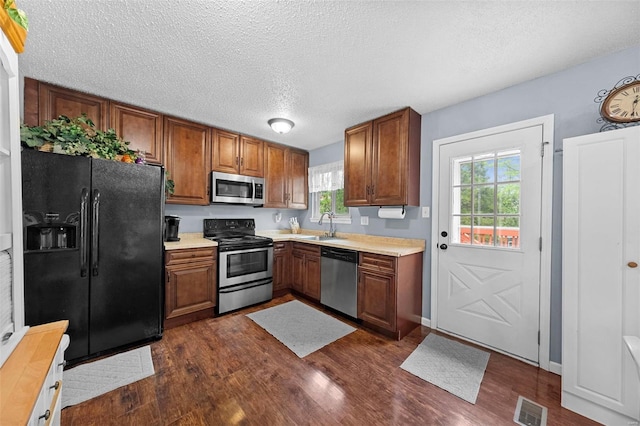 kitchen with appliances with stainless steel finishes, brown cabinetry, dark wood-style floors, and visible vents