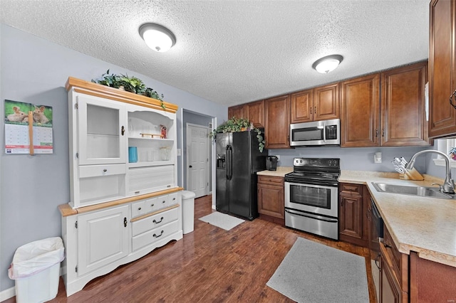 kitchen with a sink, light countertops, a textured ceiling, stainless steel appliances, and dark wood-style floors